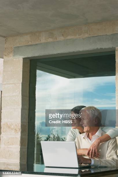 senior woman embracing husband with laptop on table outside house - premium access images stock pictures, royalty-free photos & images