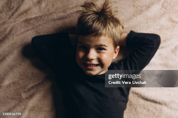 cute little boy is lying on the bed. a 4 year old boy plays on the bed. happy child. recreation. sleep. morning. - kids sleep in bed stockfoto's en -beelden