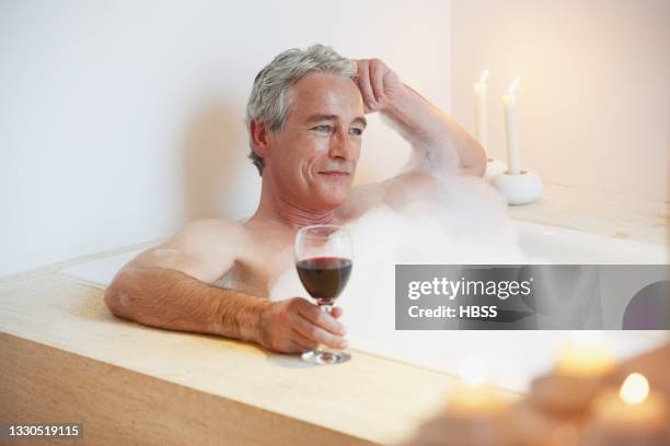 mature man enjoying a bath with glass of red wine - red tub 個照片及圖片檔