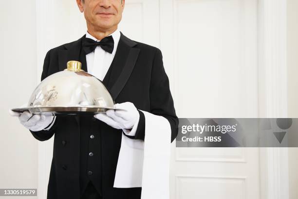 elegant butler serving meal under serving dome in luxury hotel - waiter stock-fotos und bilder