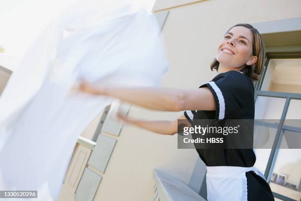 chambermaid shaking bedlinen on balcony at hotel - cleaner man uniform stock-fotos und bilder