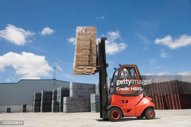 worker driving forklift on factory yard - gabelstapler stock-fotos und bilder