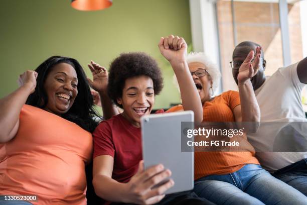 multi generation family celebrating while watching something on digital tablet at home - sport tablet stockfoto's en -beelden