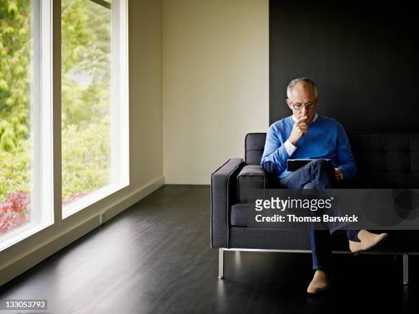 mature man sitting looking at digital tablet - mature man using digital tablet stock pictures, royalty-free photos & images