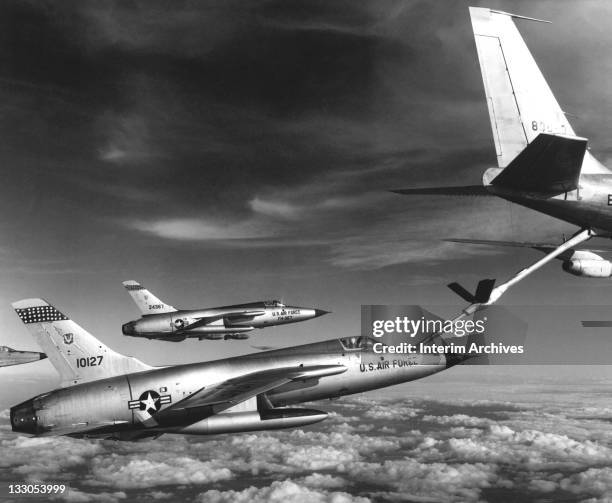 Three Air Force F-105 Thunderchief pilots guide their planes in a tight formation while re-fueling frm an Air Force KC-135 Stratotanker 'gas...