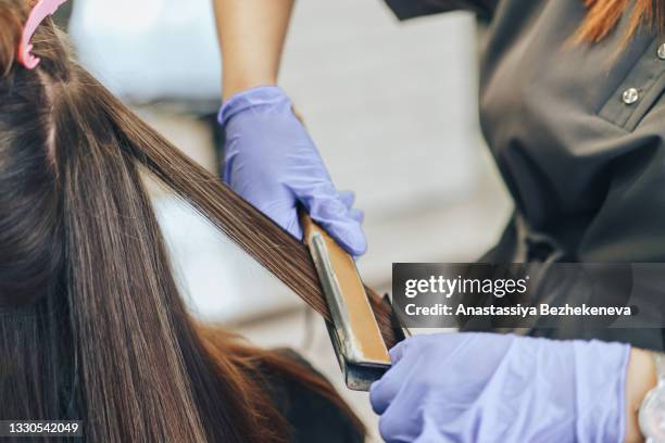 close-up of a hairdresser straightening long brown hair with hair irons - bijstellen stockfoto's en -beelden