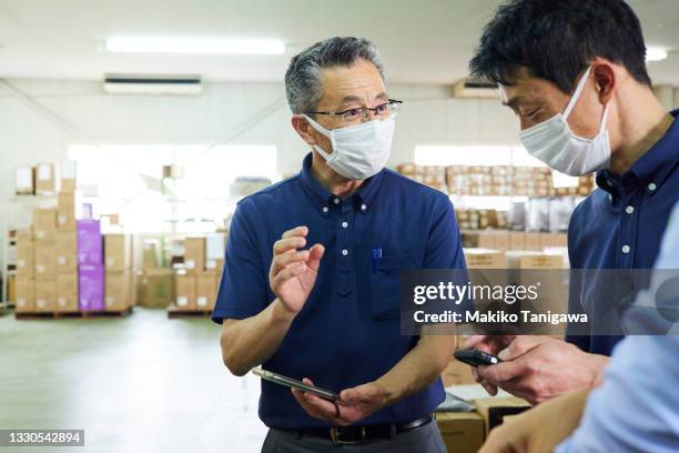 senior and middle-aged men working in a warehouse during the coronavirus pandemic - vitale beroepen stockfoto's en -beelden