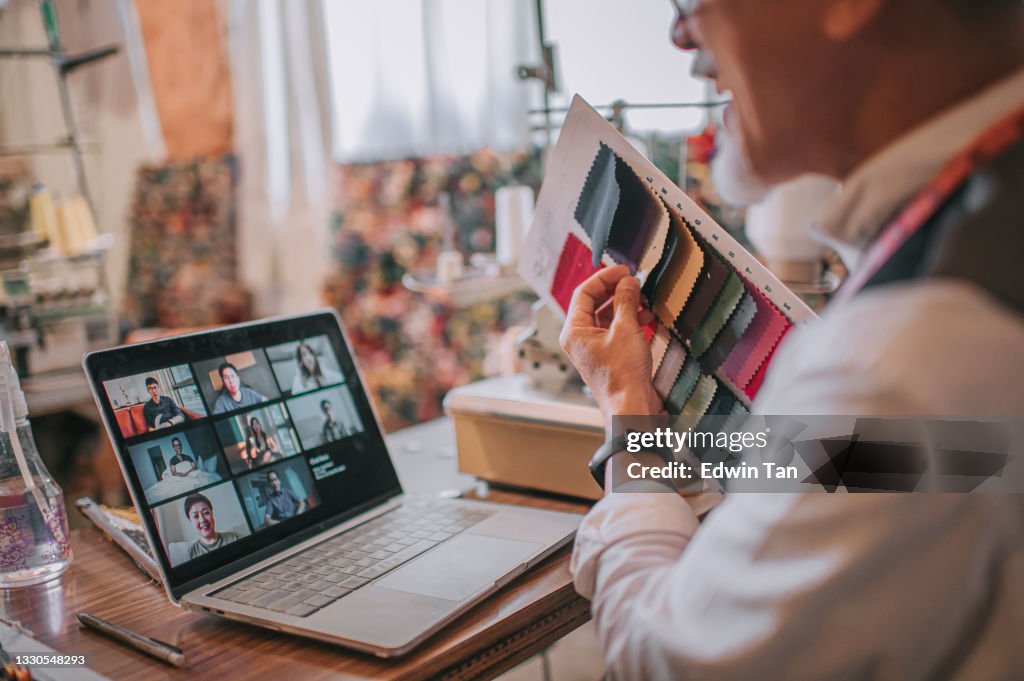 Looking over shoulder asian chinese senior man showing fabric swatch video call student with digital tablet conducting online education class at his studio