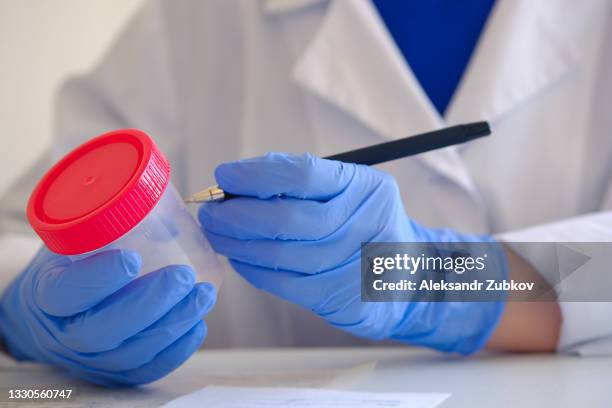 a container with a sperm analysis. nearby, a doctor's hand in medical gloves fills out documents and forms. donor sperm for artificial insemination, infertility treatment, child planning. passing an analysis for the detection of pathology. men's health. - sperm stock pictures, royalty-free photos & images