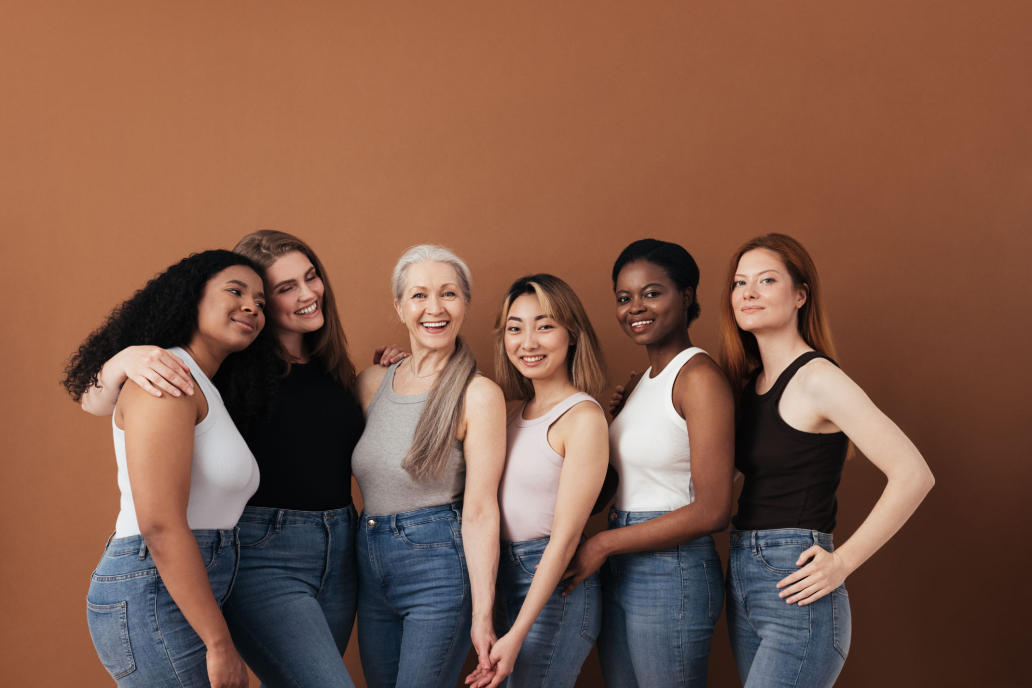 Grupo multiétnico de mulheres de diferentes idades posando contra fundo marrom olhando para a câmera Grupo multiétnico de mulheres de diferentes idades posando contra fundo marrom olhando para a câmera