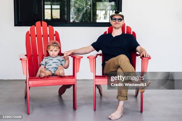 man holding hand of boy while sitting on chairs in patio during vacation - adirondack chair stockfoto's en -beelden