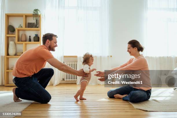 parents helping daughter walking at home - primi passi foto e immagini stock