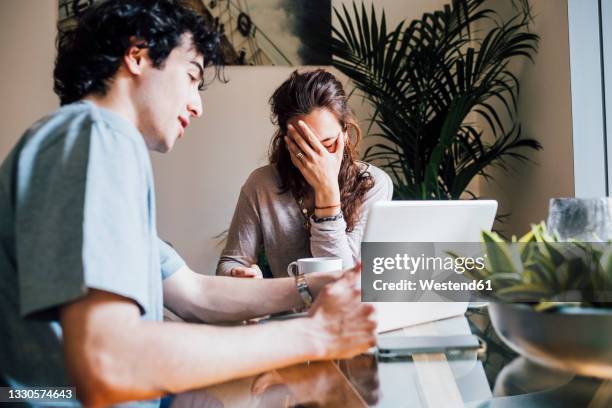 boyfriend with laptop explaining to frustrated girlfriend at home - bad romance stock pictures, royalty-free photos & images