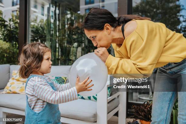 girl looking at mother blowing balloon in backyard - pusten stock-fotos und bilder