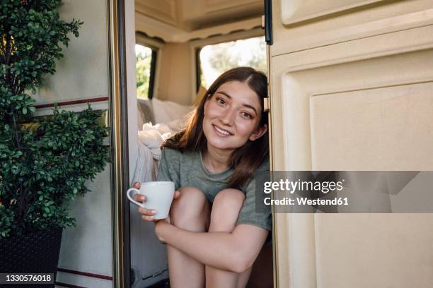beautiful woman holding coffee cup sitting at camper doorway - portrait of a camper stock pictures, royalty-free photos & images