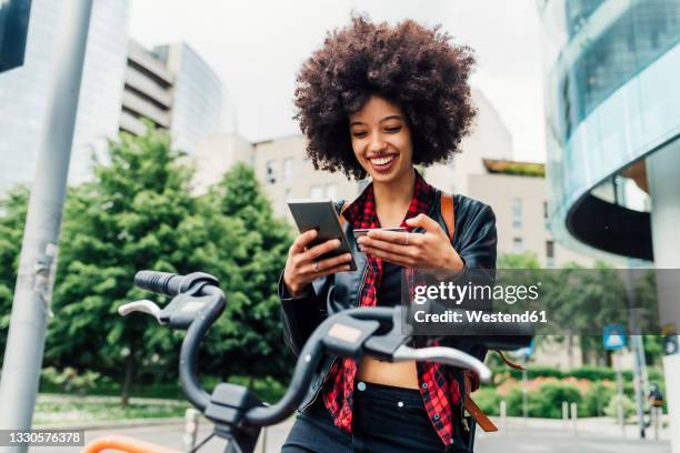 smiling woman holding credit card while using mobile phone in city - mobile banking stockfoto's en -beelden