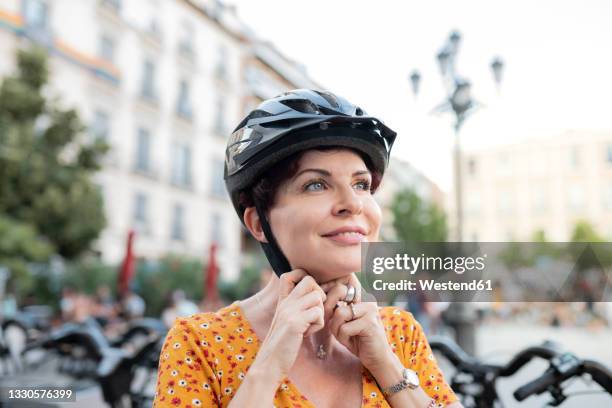 smiling woman fastening cycling helmet in city - cycling helmet photos et images de collection