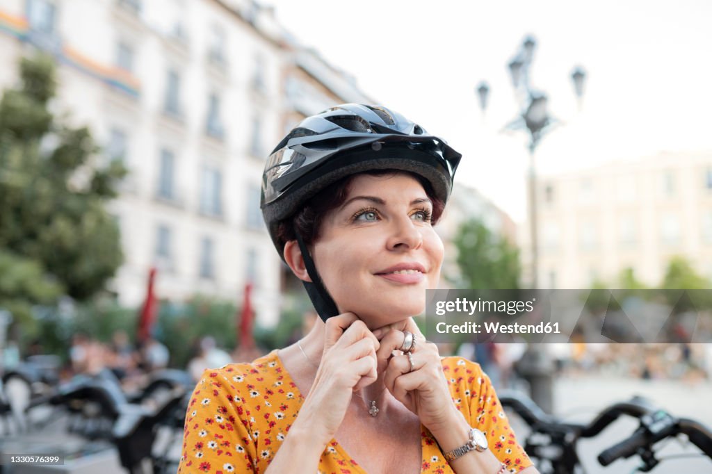 Smiling woman fastening cycling helmet in city