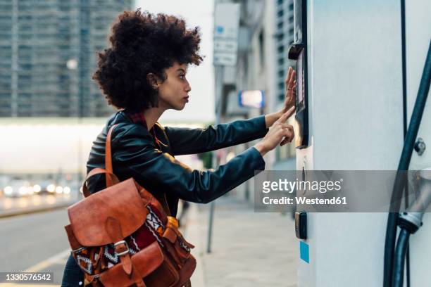 woman with backpack using ticket machine at electric vehicle charging station - people stand stock-fotos und bilder