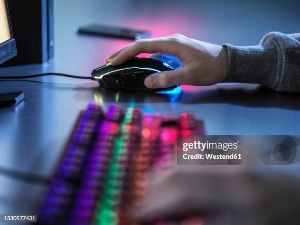 boy using illuminated gaming mouse while playing video game - computer mouse table stock-fotos und bilder