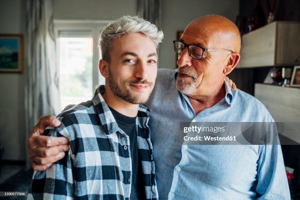 Father with arm around looking at son while standing at home