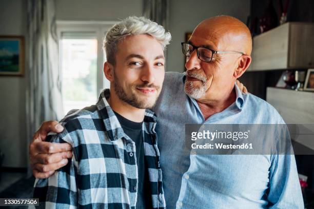 father with arm around looking at son while standing at home - figlio maschio foto e immagini stock
