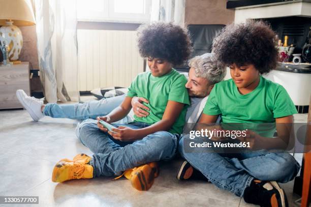 young man with twin brothers using smart phone while sitting at home - multiple birth stock pictures, royalty-free photos & images