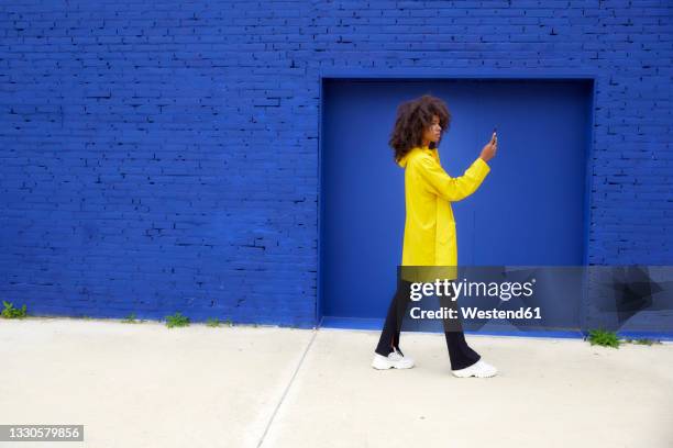 young woman text messaging through smart phone by blue wall - afro stock pictures, royalty-free photos & images