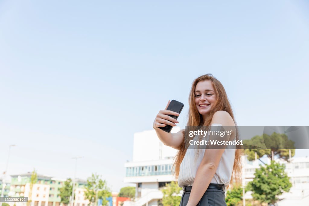 Smiling businesswoman taking selfie through mobile phone after taking vaccination in front of sky