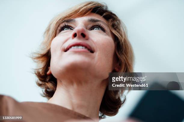 businesswoman with mobile phone looking away in office - looking up stock-fotos und bilder