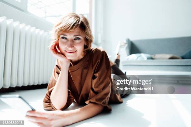 smiling businesswoman with hand on chin holding mobile phone in office - allongé sur le devant photos et images de collection