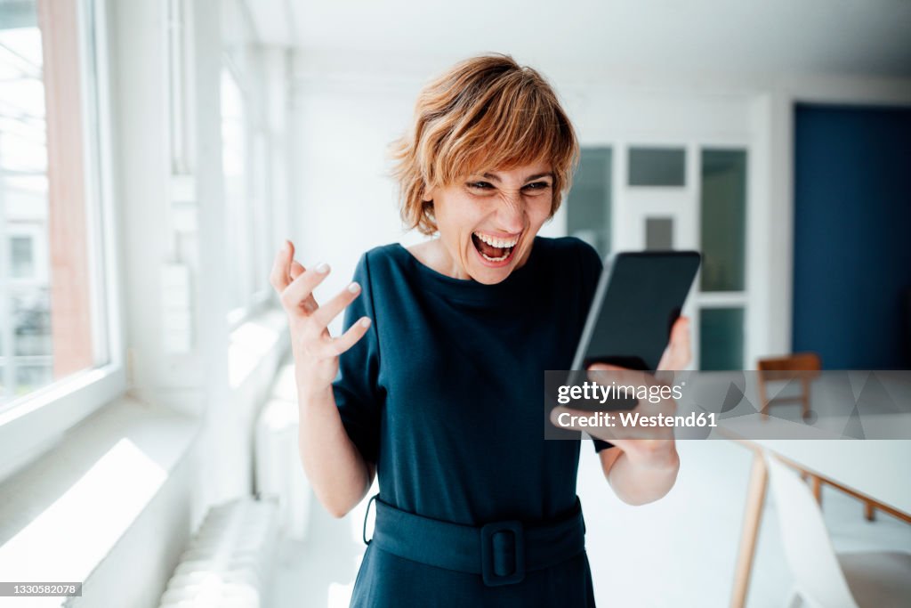 Excited businesswoman using mobile phone while standing in office