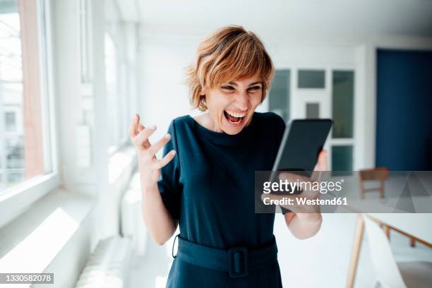 excited businesswoman using mobile phone while standing in office - joy stock-fotos und bilder