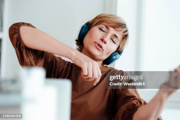 businesswoman day dreaming while listening music through headphones in office - music stock-fotos und bilder