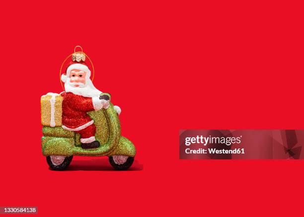 christmas ornament of santa claus riding motor scooter against vibrant red background - santa riding stock pictures, royalty-free photos & images