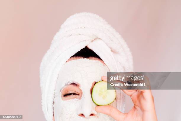 young woman with beauty face mask covering eye with cucumber slice - cucumber eye mask stock pictures, royalty-free photos & images
