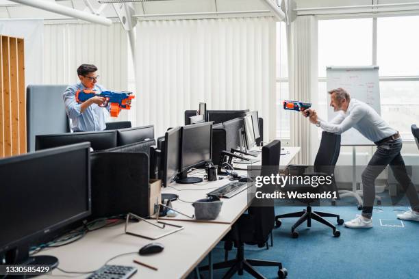 male colleagues playing with toy gun while standing by desk - arma de brinquedo imagens e fotografias de stock