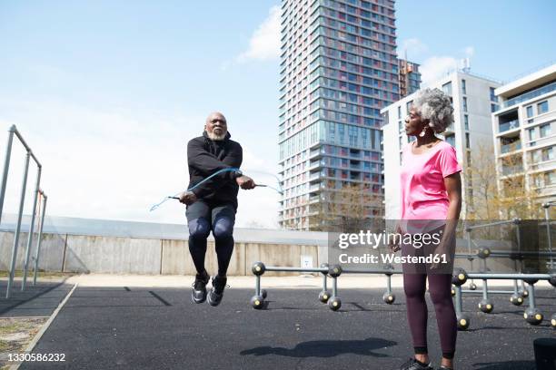 man skipping rope by woman at park on sunny day - skip stockfoto's en -beelden