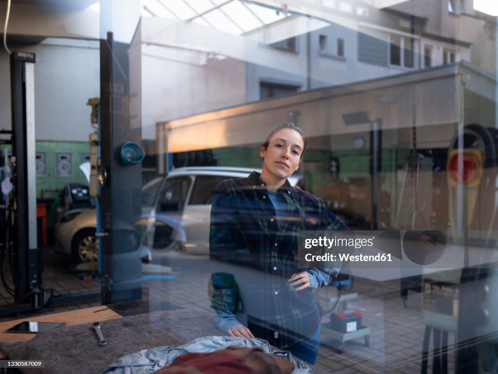 Female mechanic standing at car repair shop seen through window