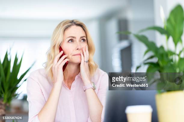 contemplating businesswoman talking on smart phone at home office - worry stock-fotos und bilder