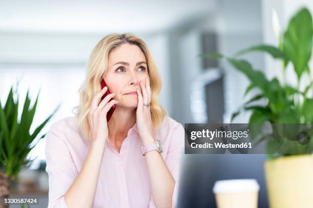 contemplating businesswoman talking on smart phone at home office - woman concerned stockfoto's en -beelden