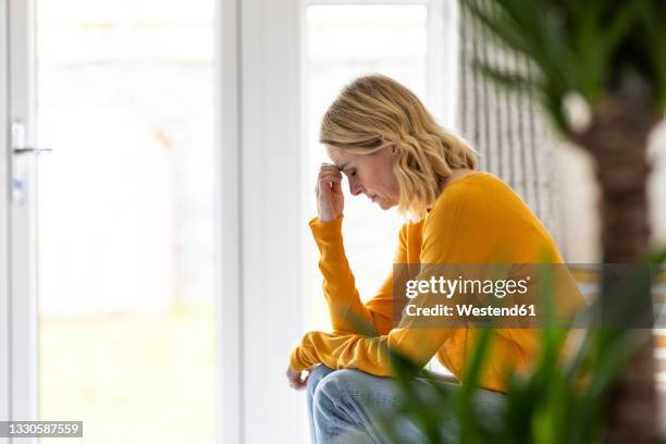 depressed mature woman sitting at home - mal di testa foto e immagini stock