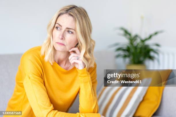 thoughtful woman looking away while sitting at home - tristezza foto e immagini stock