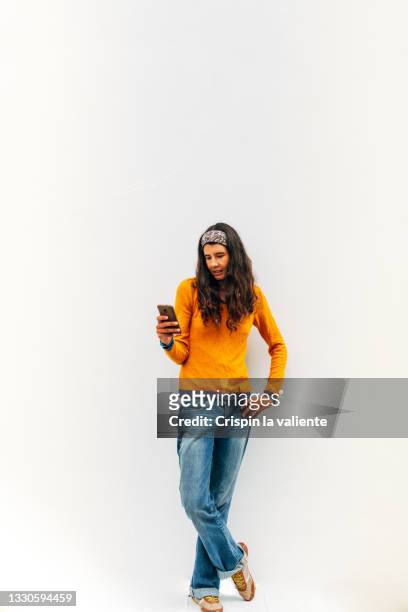 full-length shot of young woman using her smartphone on white background. the woman has long hair and wears casual clothes - sitting and using smartphone studio stockfoto's en -beelden
