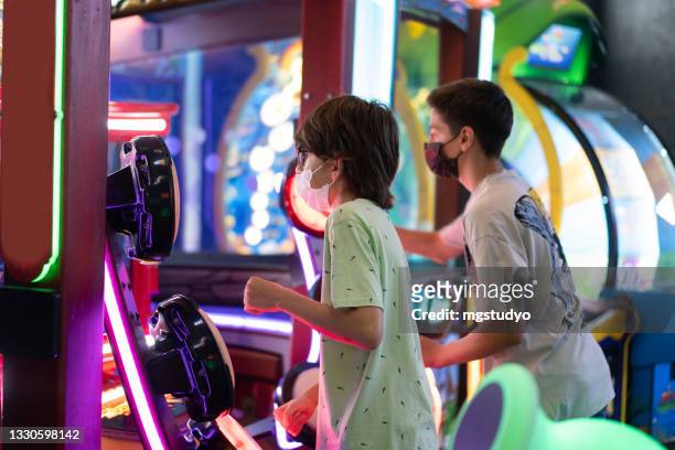 happy young friends playing arcade game machine - arcade machine stockfoto's en -beelden