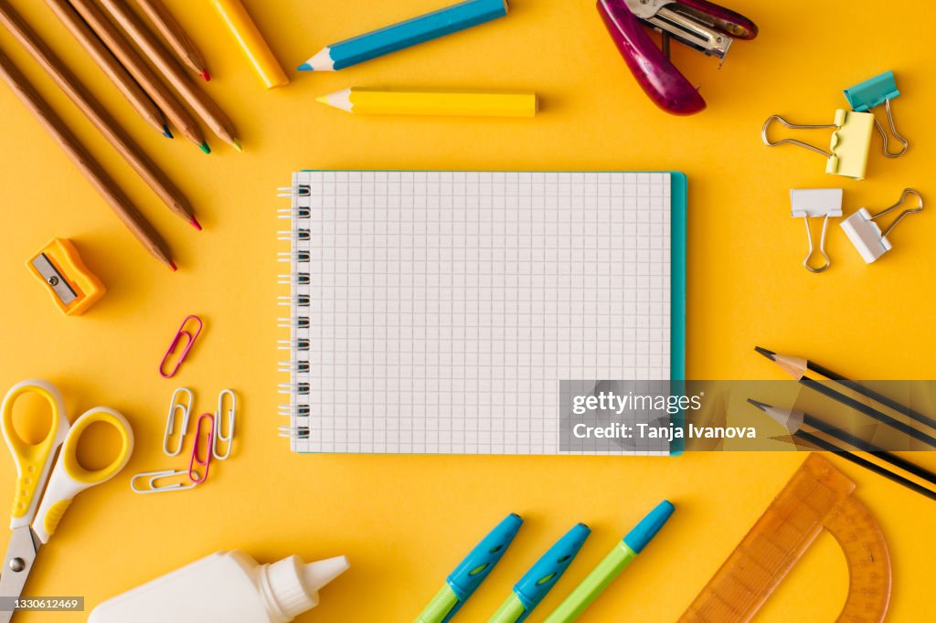 Back to school concept. Creative composition of school stationery white sheet of notebook paper on a yellow background. Top view, flat lay, copy space.