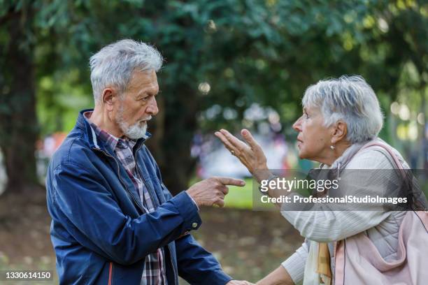 a senior man and his wife are having a serious discussion in a public park. - angry coworker stock pictures, royalty-free photos & images