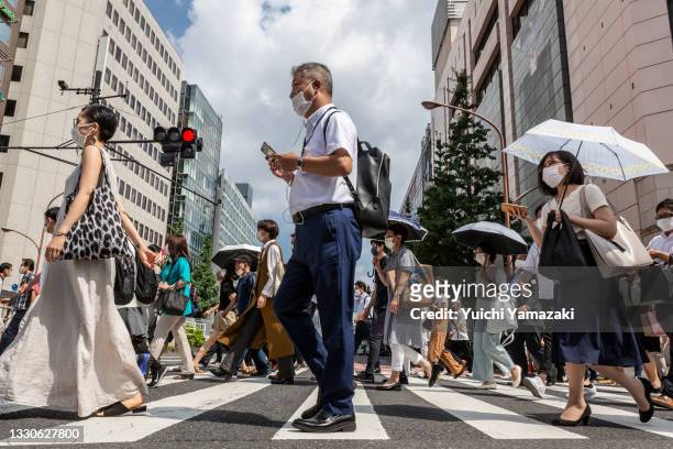 Commuters wearing face masks cross a street in Shinjuku area on July 26, 2021 in Tokyo, Japan. Despite draconian restrictions on athletes and...