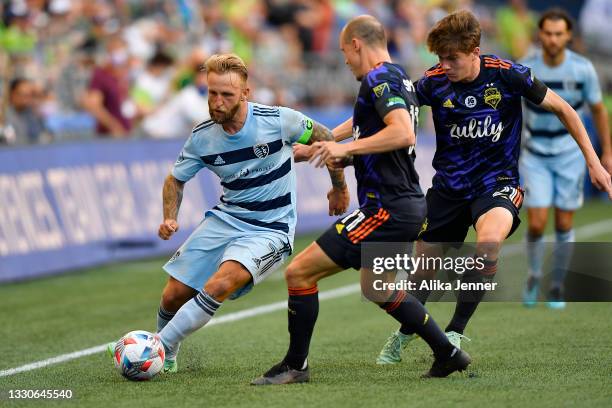 Johnny Russell of Sporting Kansas City moves the ball against Brad Smith and Reed Baker-Whiting of Seattle Sounders at Lumen Field on July 25, 2021...