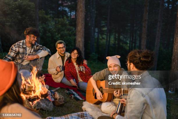 glückliche frau, die ihren freunden auf dem campingplatz am lagerfeuer gitarre spielt - holzfeuer stock-fotos und bilder